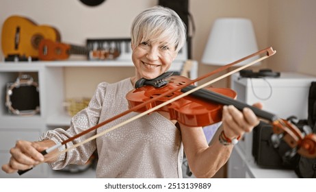 Smiling mature woman with grey hair playing violin indoors with musical instruments background. - Powered by Shutterstock