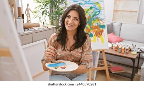 A smiling mature woman holding a palette while painting on a canvas in a bright art studio. - Powered by Shutterstock