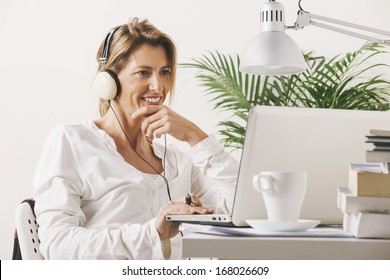 Smiling mature woman listening music with headphones. / Mature businesswoman working with laptop at home. - Powered by Shutterstock