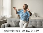 Smiling mature woman moves to favourite song in living room, enjoy active leisure alone at home entertaining, having fun, dancing energetically, exude happiness and carelessness, relish retired life