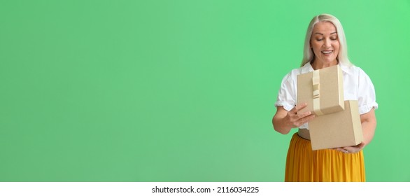 Smiling Mature Woman Opening Gift Box On Green Background With Space For Text. International Women's Day Celebration