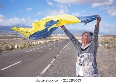 Smiling Mature Woman Outdoors In Countryside Waving A Ukraine Flag Scarf In The Wind. Caucasian Senior Woman With Short Hair Wearing Eyeglasses. Stop War And Make Peace In The World