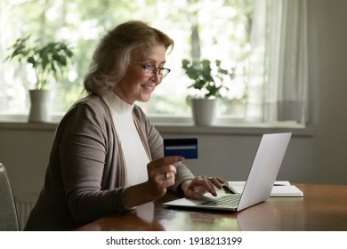 Smiling mature woman paying online by credit card, using laptop, looking at screen, happy satisfied elderly customer shopping, browsing internet banking service, checking balance, secure payment - Powered by Shutterstock