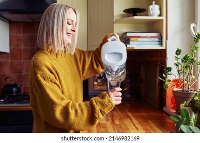 Smiling mature woman pouring filtered water into glass at kitchen - Shutterstock ID 2146982169