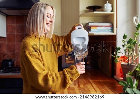 Smiling mature woman pouring filtered water into glass at kitchen