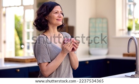 Smiling Mature Woman Standing In Kitchen Relaxing With Cup Of Coffee