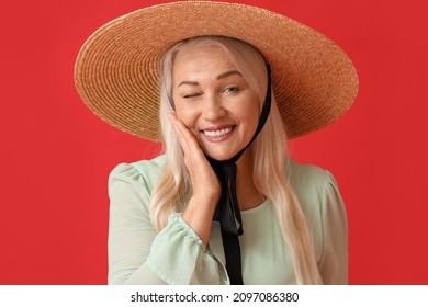 Smiling Mature Woman In Straw Hat Winking On Red Background