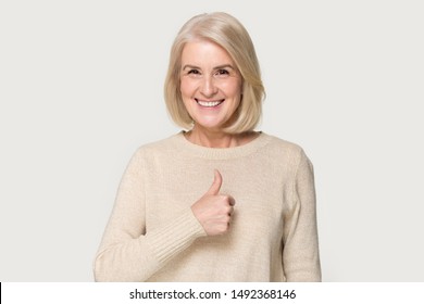 Smiling mature woman in sweater isolated on grey studio background show thumbs up recommend service, happy positive senior lady give sincere recommendation, advice good or sale offer - Powered by Shutterstock