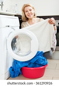 Smiling Mature Woman Using Washing Machine At Home Laundry