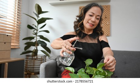 Smiling Mature Woman Watering Houseplants In Living Room. Housework And Plants Care Concept