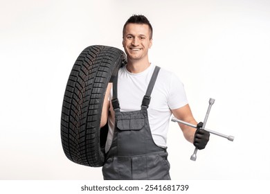 Smiling mechanic holding a tire and lug wrench, ready for a tire change, isolated on white background - Powered by Shutterstock