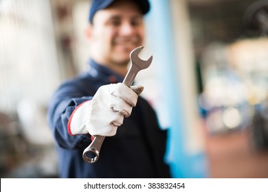 Smiling mechanic holding a wrench in his shop - Shutterstock ID 383832454