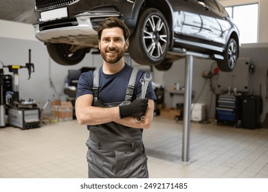 Smiling mechanic holding wrench in modern auto repair shop with car on lift. Confident professional in uniform ready for vehicle maintenance and repair services in clean workshop environment. - Powered by Shutterstock