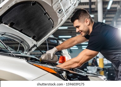 smiling mechanic pouring motor oil at car engine