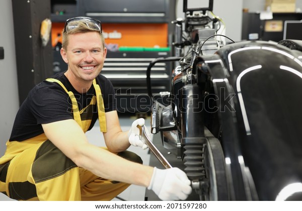 Smiling\
mechanic spinning motorcycle wheel with wrench in work shop.\
Maintenance of cars and motorcycles\
concept