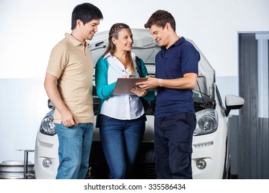 Smiling mechanic taking sign on document from customers in garage - Powered by Shutterstock