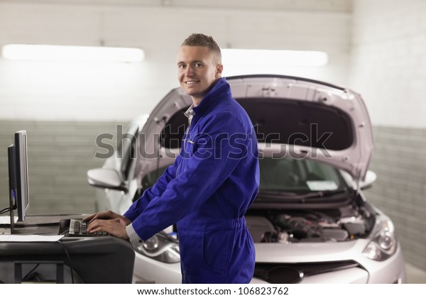 Smiling\
mechanic typing on a computer in a\
garage