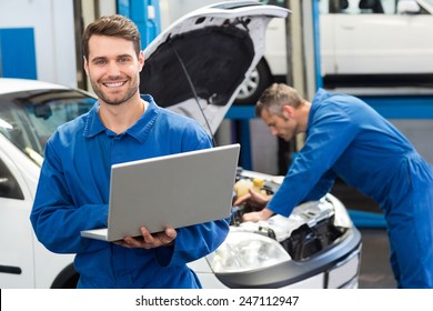 Smiling mechanic using a laptop at the repair garage