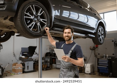 Smiling mechanic using tablet in auto repair shop with car on lift. Confident male technician diagnosing vehicle problem using modern technology. Professional car service in well-equipped garage. - Powered by Shutterstock