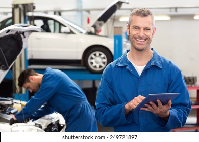 Smiling mechanic using a tablet pc at the repair garage - Powered by Shutterstock