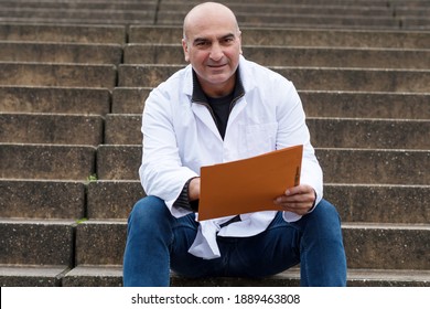 Smiling Medical Doctor Or Dentist Sitting On Outdoor Stairs And Holding A Clinical Study Report