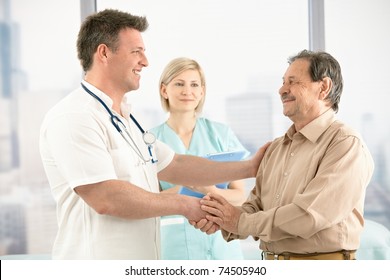 Smiling Medical Doctor Shaking Hands With Happy Senior Patient, Nurse In Background.?