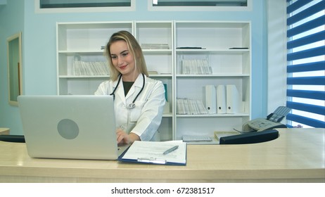 Smiling Medical Nurse Working On Laptop And Making Notes At Reception Desk