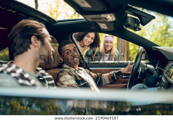 Smiling men in\
a car talking to girls on the\
road