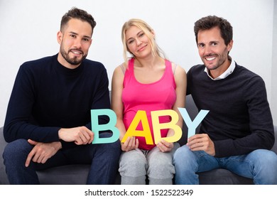 Smiling Men Touching The Belly Of Pregnant Surrogate Woman Holding Baby Word Letters