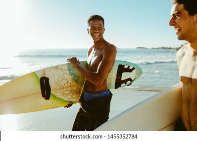 Smiling men walking on the beach carrying surfboards. Male friends on surfing vacation at the sea.