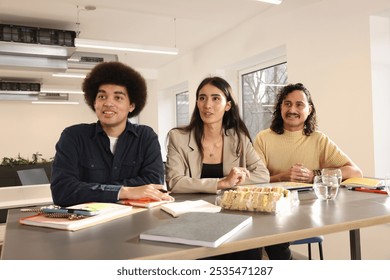 Smiling men and woman sitting at table with laptop, glasses and sandwiches during meeting in modern creative office - Powered by Shutterstock