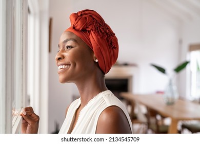 Smiling mid adult african american woman with turban looking outside the window. Cheerful black mature woman wearing traditional headscarf while contemplating. Happy middle aged lady thinking. - Powered by Shutterstock