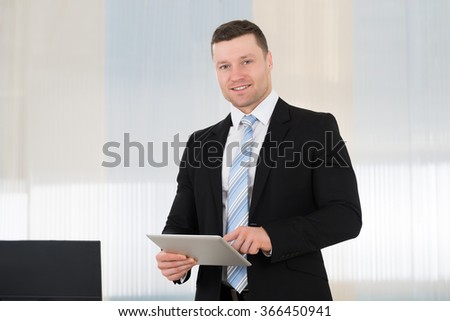 Smiling mid adult businessman using digital tablet while standing in office