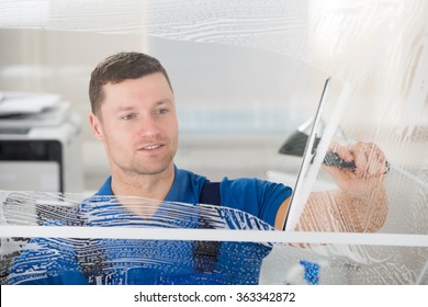 Smiling mid adult worker cleaning soap sud on glass window with squeegee