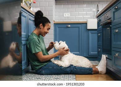 Smiling Mid Aged African Woman Playing With Her Dog In The Kitchen