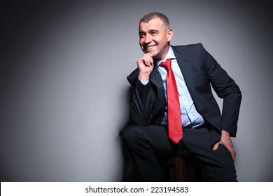 Smiling Mid Aged Business Man Sitting On A Stool Holding His Hand To The Chin, Looking Away.