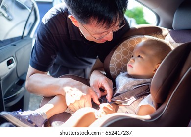 Smiling Middle age asian father helps his cute little asian 1 year old toddler baby boy child to fasten belt on car seat in car before driving, happy traveling with child concept