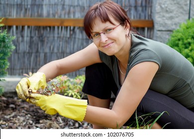 Smiling Middle Age Woman Gardener With Flowers Outdoor In Her Garden
