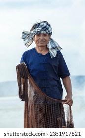 Smiling middle aged Asian fisherman with fishing net on lake in Thailand.