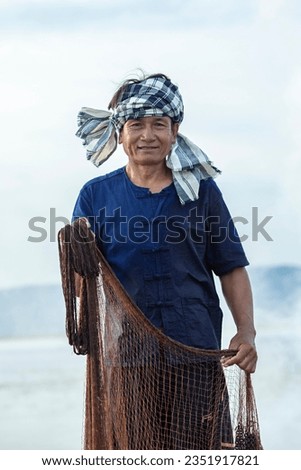 Smiling middle aged Asian fisherman with fishing net on lake in Thailand.