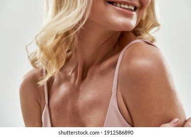 Smiling middle aged blond caucasian woman posing with naked shoulder against light background, cropped. Authentic woman beauty concept