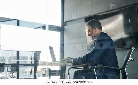 Smiling middle aged business man executive ceo sitting at desk using laptop. Happy professional businessman manager working on computer technology in office. View through glass. - Powered by Shutterstock