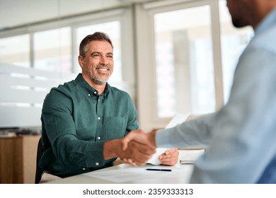 Smiling middle aged business man handshaking partner making partnership collaboration agreement at office meeting, hr manager and new worker shake hands recruiting at job interview. Welcome onboarding - Powered by Shutterstock