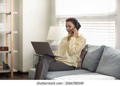 Smiling middle aged business woman freelancer entrepreneur enjoying phone call conversation, working distantly on computer, sitting on cozy couch in modern living room or office, multitask concept. - Powered by Shutterstock