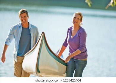 Smiling Middle Aged Couple Carrying Their Canoe Away From A Lake.