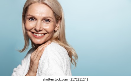 Smiling Middle Aged Female Model With Wrinkles, Nourished, Glowing Facial Skin, Moisturized Face, Looking Happy At Camera, Blue Background