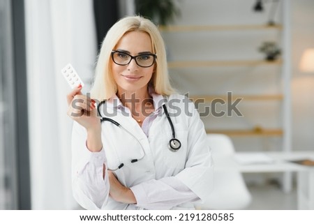 Smiling middle aged female therapist in white uniform holds pills