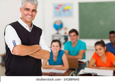 Smiling Middle Aged High School Teacher With Arms Folded Standing In Front Of The Class