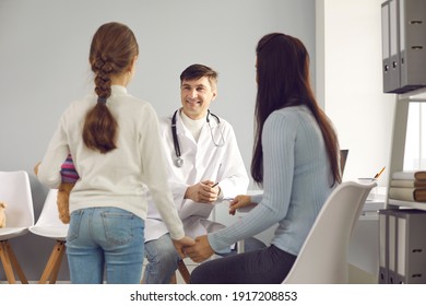 Smiling middle aged man doctor pediatrician sitting and listening to small girl and mother patients complaints during visit in medical clinic office. Medicare for kids and family doctor concept