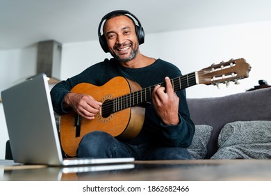 Smiling Middle Aged Man Playing Guitar At Home And Taking Online Lessons